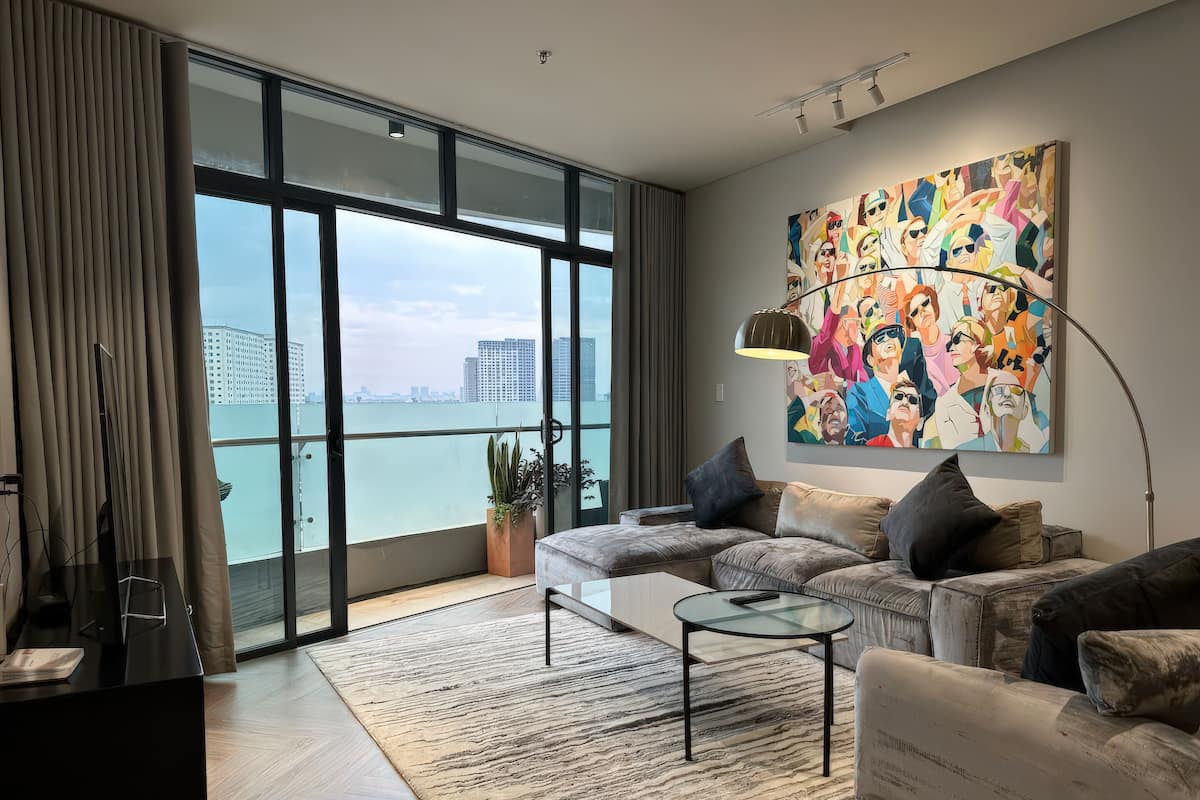 A modern living room with a large window, a sofa, a coffee table, and a painting on the wall.