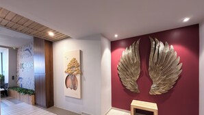 A modern hotel lobby with a wooden reception desk, a wall-mounted artwork of a tree, and a large golden wing sculpture.
