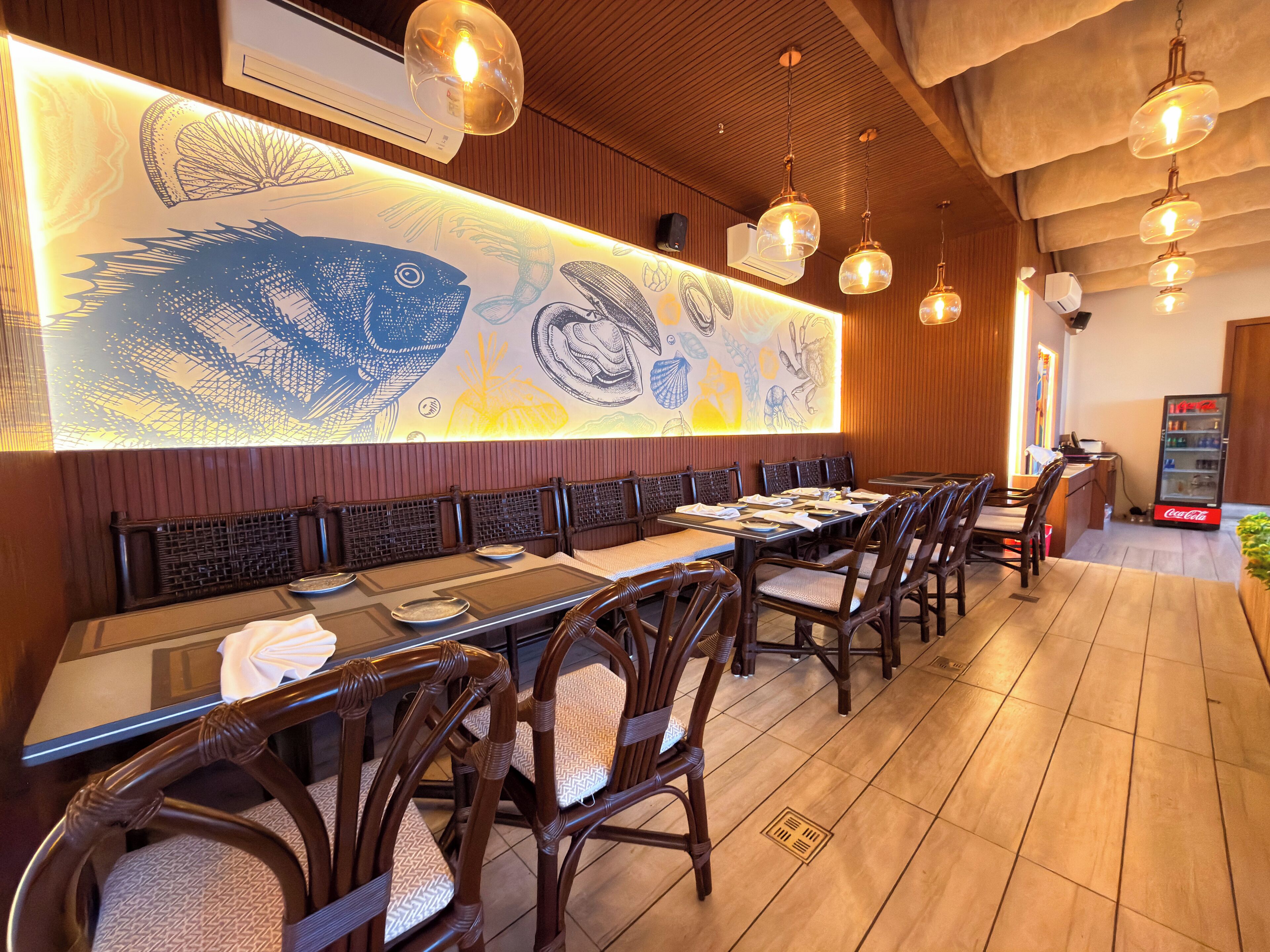 A restaurant with wooden paneling, a long communal table, and hanging pendant lights.