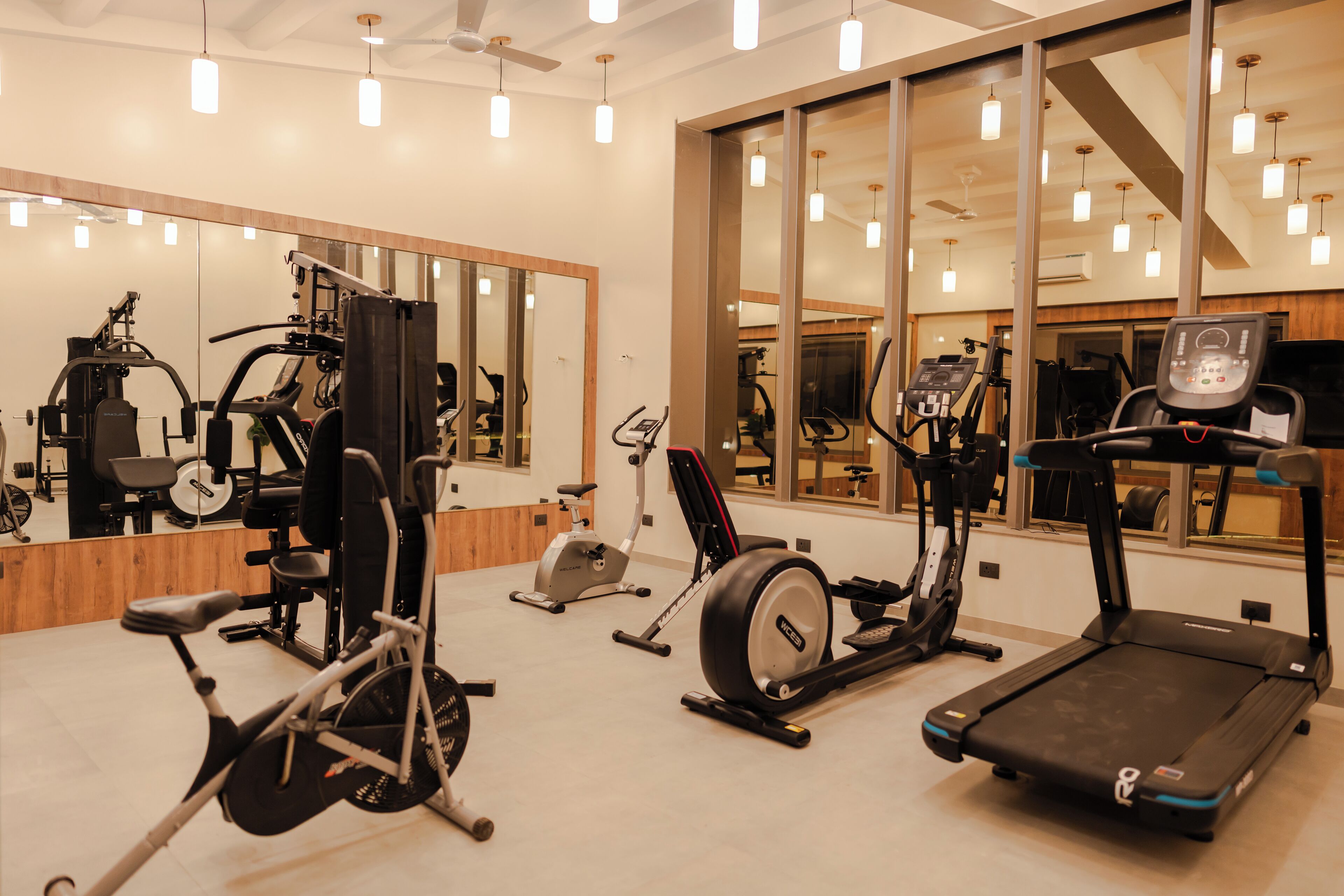 A gym with various exercise equipment, large mirrors, and pendant lighting.