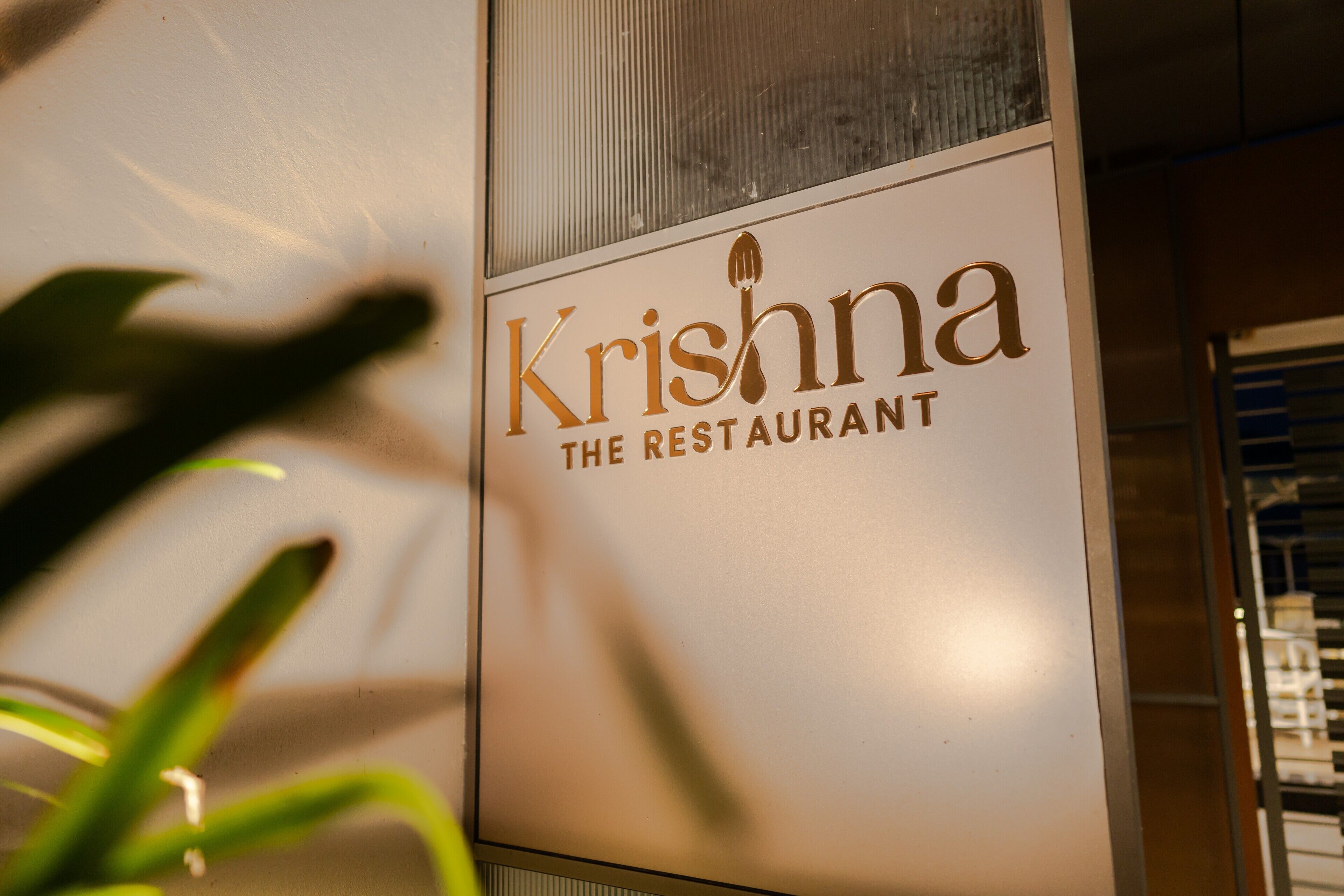 A sign for "Krishna The Restaurant" with a modern design and a metallic finish.