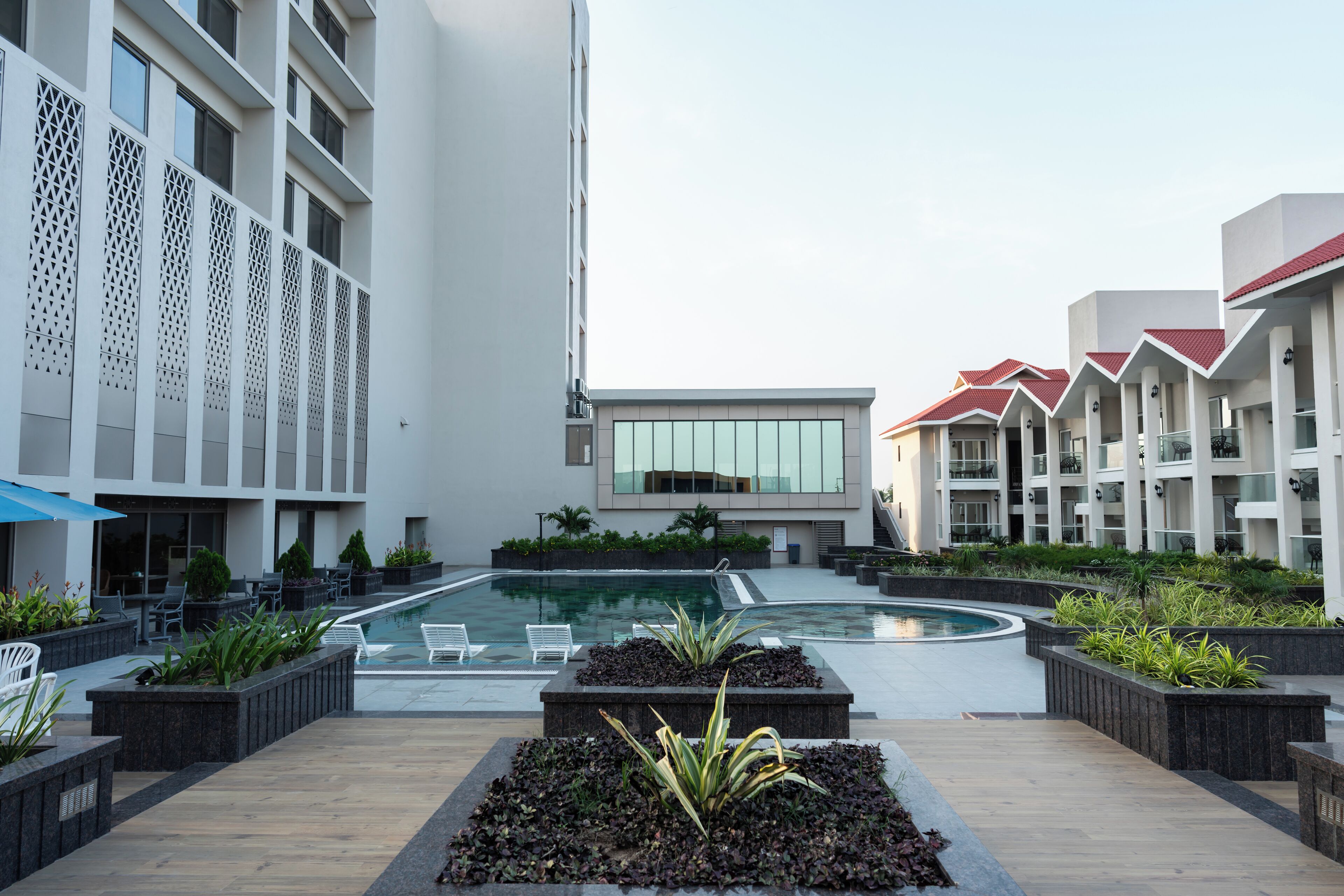 A modern hotel courtyard with a central swimming pool, outdoor seating, and a landscaped garden area.