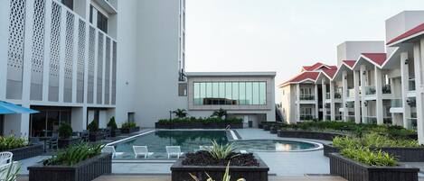 A modern hotel courtyard with a central swimming pool, outdoor seating, and a landscaped garden area.