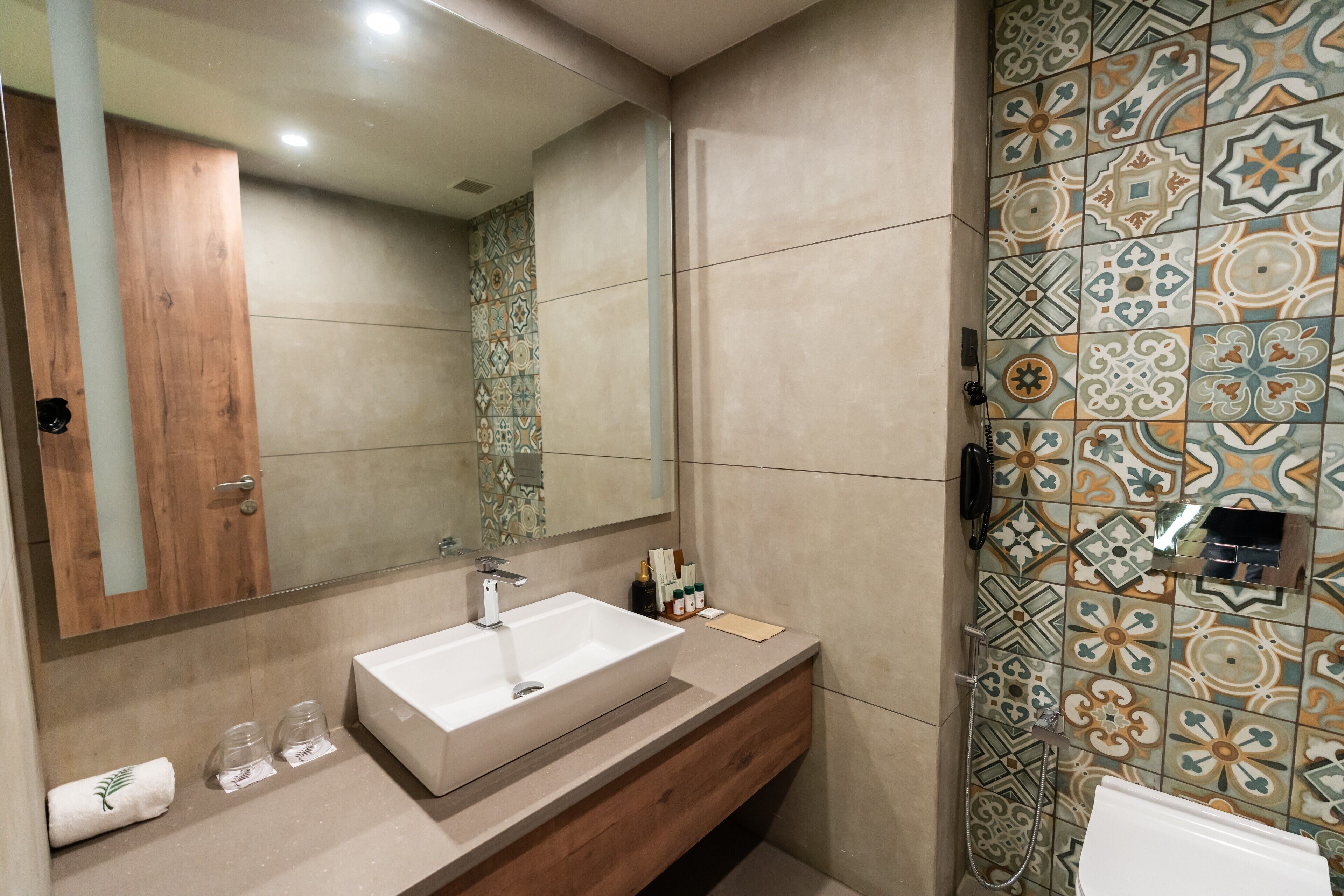 A bathroom with a large mirror, a sink, a wooden vanity, and a shower with patterned tiles.