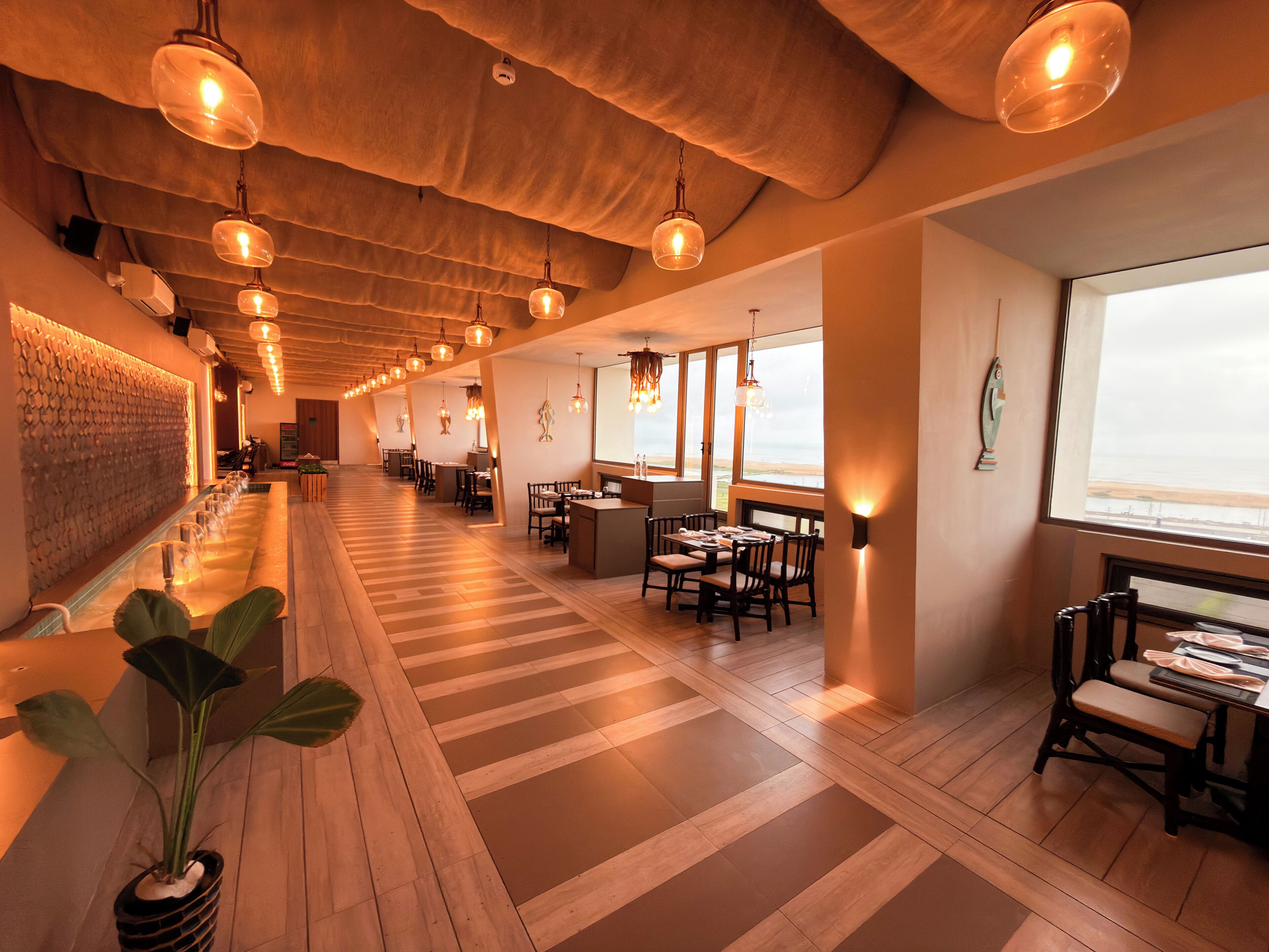 A modern restaurant with a long counter, wooden flooring, and pendant lighting.