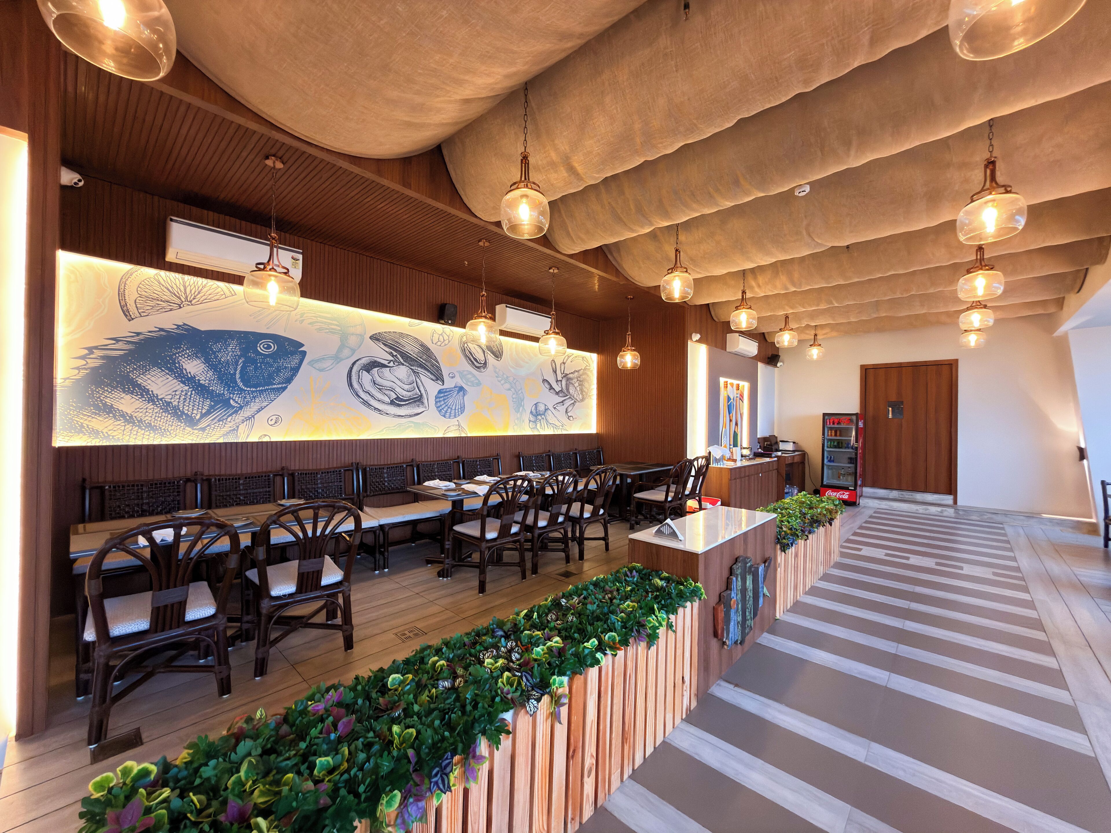 A restaurant with wooden panel walls, hanging pendant lights, and a long counter with chairs.