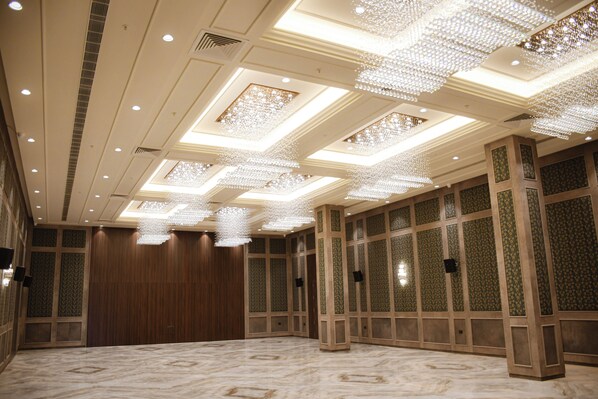 A spacious hotel room with a high ceiling, ornate chandeliers, and a marble floor.