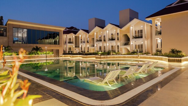 A modern hotel with a swimming pool, multiple balconies, and well-lit outdoor areas.
