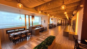 A restaurant with wooden flooring, tables, and chairs arranged for dining. Large windows provide a view of the outdoors.