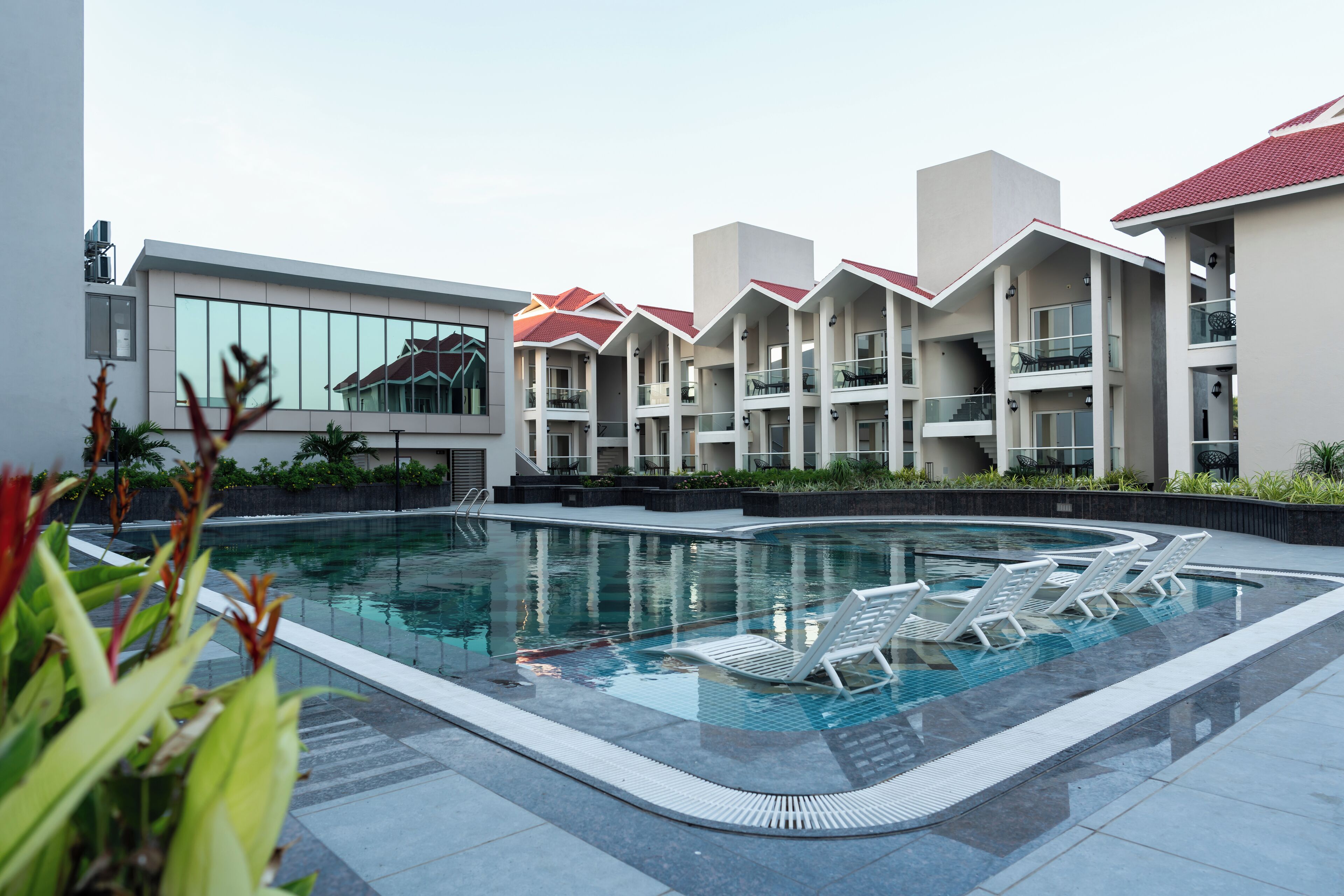 A swimming pool with lounge chairs, surrounded by a building with multiple balconies and a modern design.