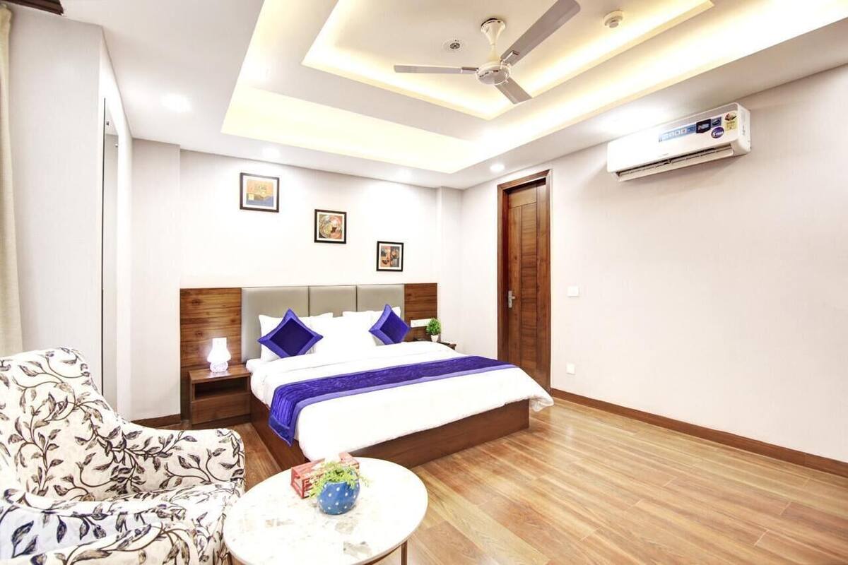 A hotel room with a bed, bedside table, lamp, chair, and a small table with a plant.