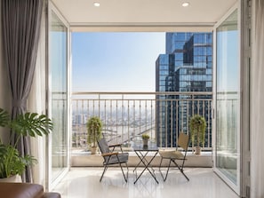 A balcony with a view of a cityscape, two chairs, a small table, and potted plants.