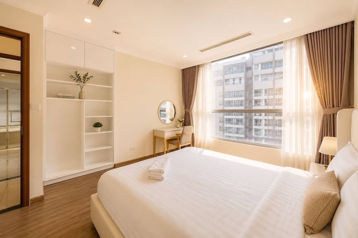 A hotel room with a bed, a desk, a mirror, a wardrobe, and a window with a city view.