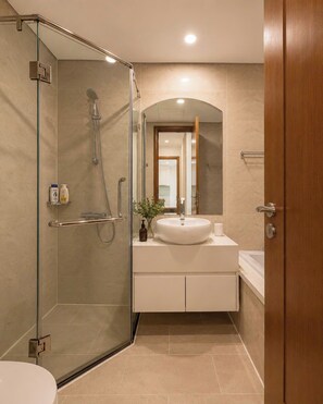 A modern bathroom with a glass-enclosed shower, a white sink, and a wooden door.
