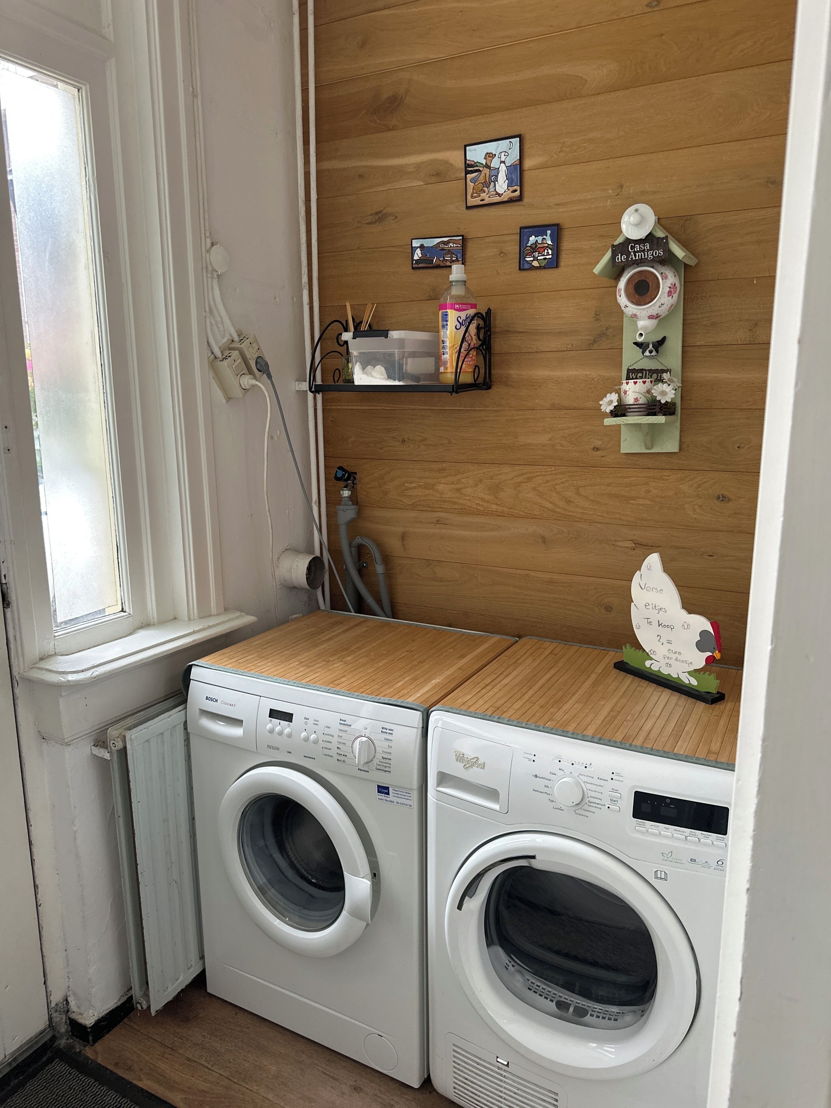 Un espace buanderie comprenant deux machines à laver, une étagère en bois avec divers objets, et une nichoir fixé au mur.