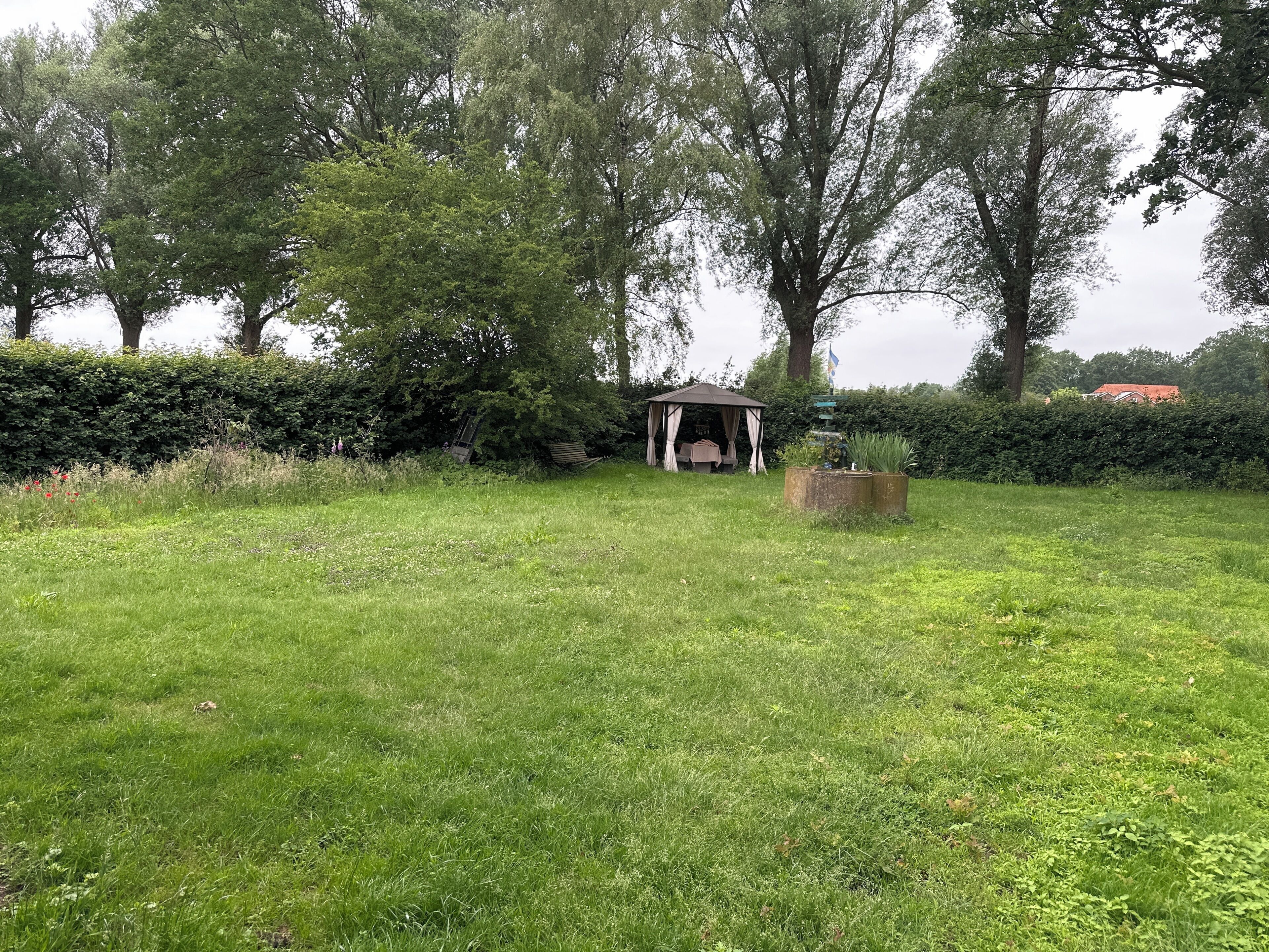 A grassy outdoor area with a gazebo, a small table, and a planter.