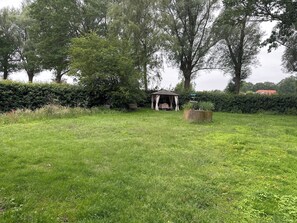 A grassy outdoor area with a gazebo, a small table, and a planter.