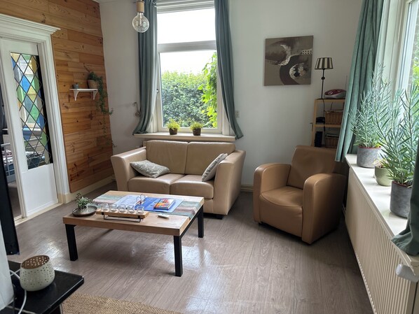 A living room with a sofa, armchair, coffee table, and potted plants.