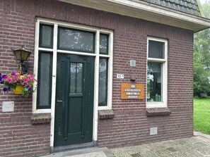 A brick building with a green door, two windows, and a welcome sign.