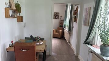 A cozy living room with a dining area, a comfortable chair, a potted plant, and a view through a window.