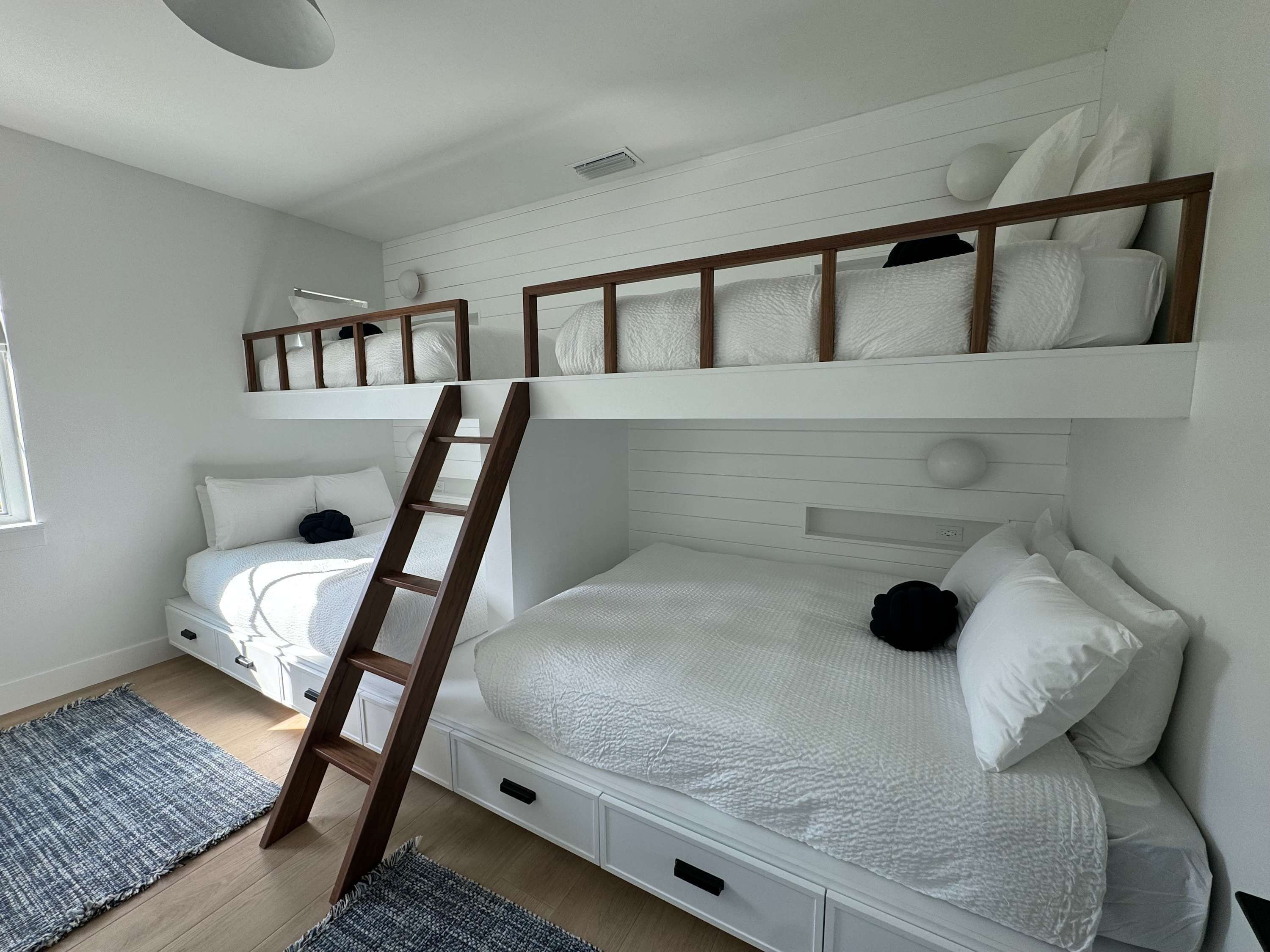 A bunk bed room with a wooden ladder, white bedding, and a gray rug on the floor.