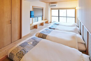 Habitación de hotel con cuatro camas alineadas, un televisor montado en la pared y un ventanal con vistas al exterior.