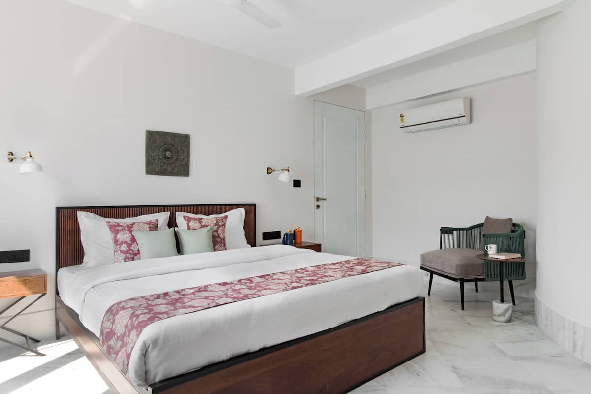 Un dormitorio moderno con una cama grande, una mesita de noche, una silla y un equipo de aire acondicionado en la pared.
