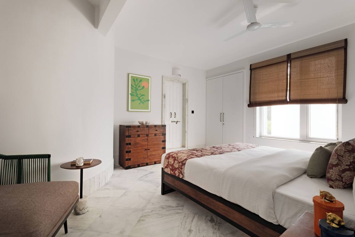 Un dormitorio con una cama, un tocador, una silla, una mesita y una ventana con persianas.