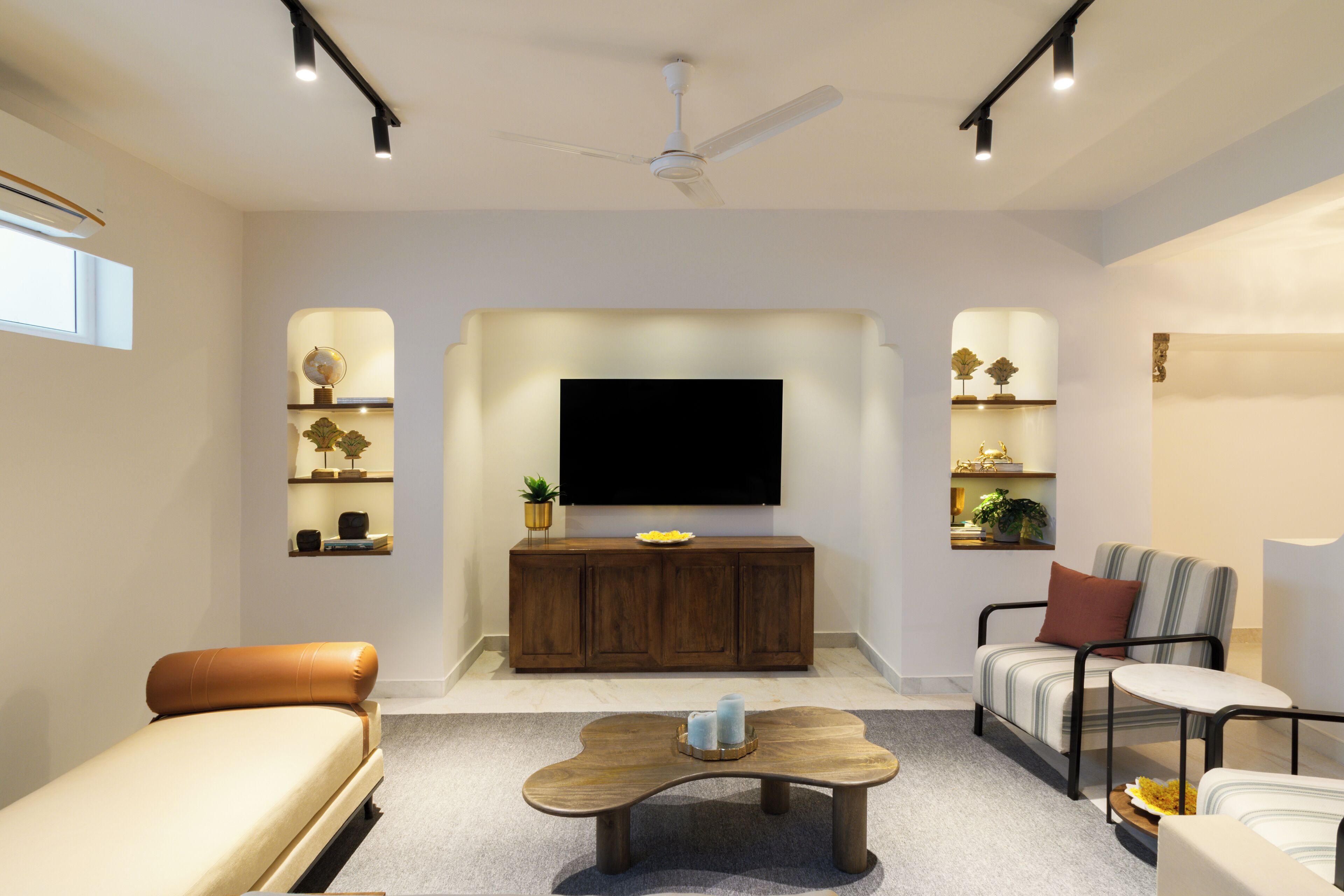 A modern living room with a flat-screen TV, wooden cabinet, sofa, armchair, and coffee table.