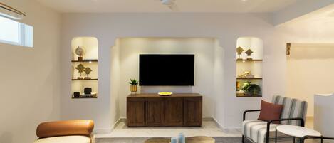 A modern living room with a flat-screen TV, wooden cabinet, sofa, armchair, and coffee table.