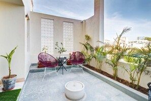 A small outdoor patio with two purple chairs, a table, and a white table lamp. There are potted plants and a decorative screen in the background. - Avaanti Boutique Stay By Avaanti Stays (Udaipur)