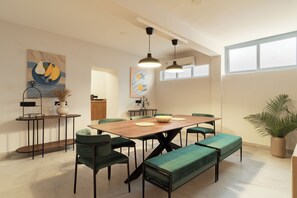 A modern dining area with a wooden table, green upholstered chairs, and a bench. There are pendant lights above the table, and artwork is displayed on the walls. - Avaanti Boutique Stay By Avaanti Stays (Udaipur)