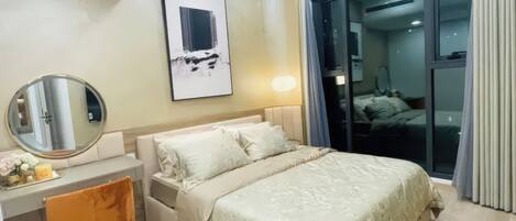 A modern hotel room with a bed, a desk, a chair, a round mirror, and a large window.