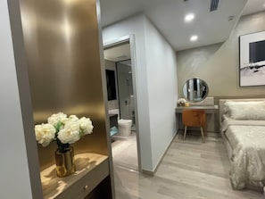 A modern bedroom with a bed, a vanity with a mirror, and a vase of flowers.