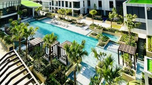 Um edifício moderno de vários andares com piscina no terraço e vegetação ao redor.