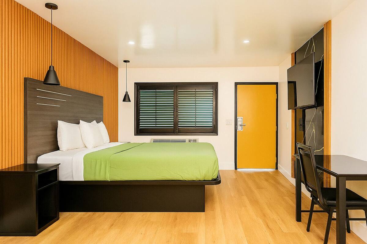 Una habitación de hotel moderna con cama, mesita de noche, escritorio, silla, televisor y ventana con persianas.