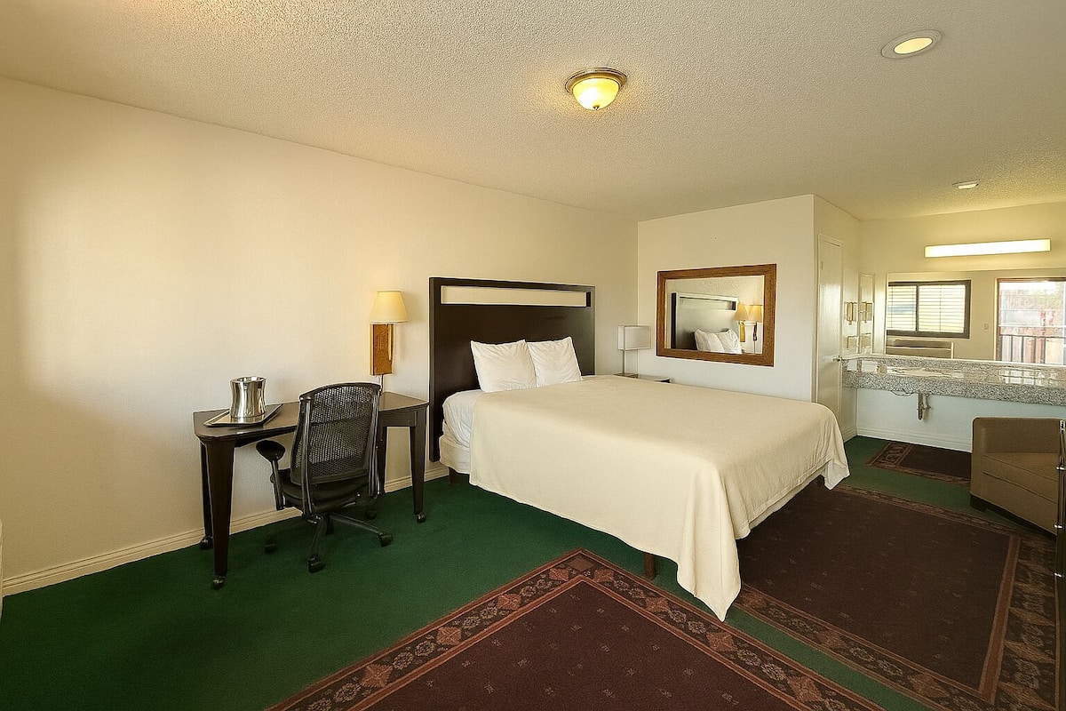 Una habitación de hotel con cama, escritorio, silla y espejo.