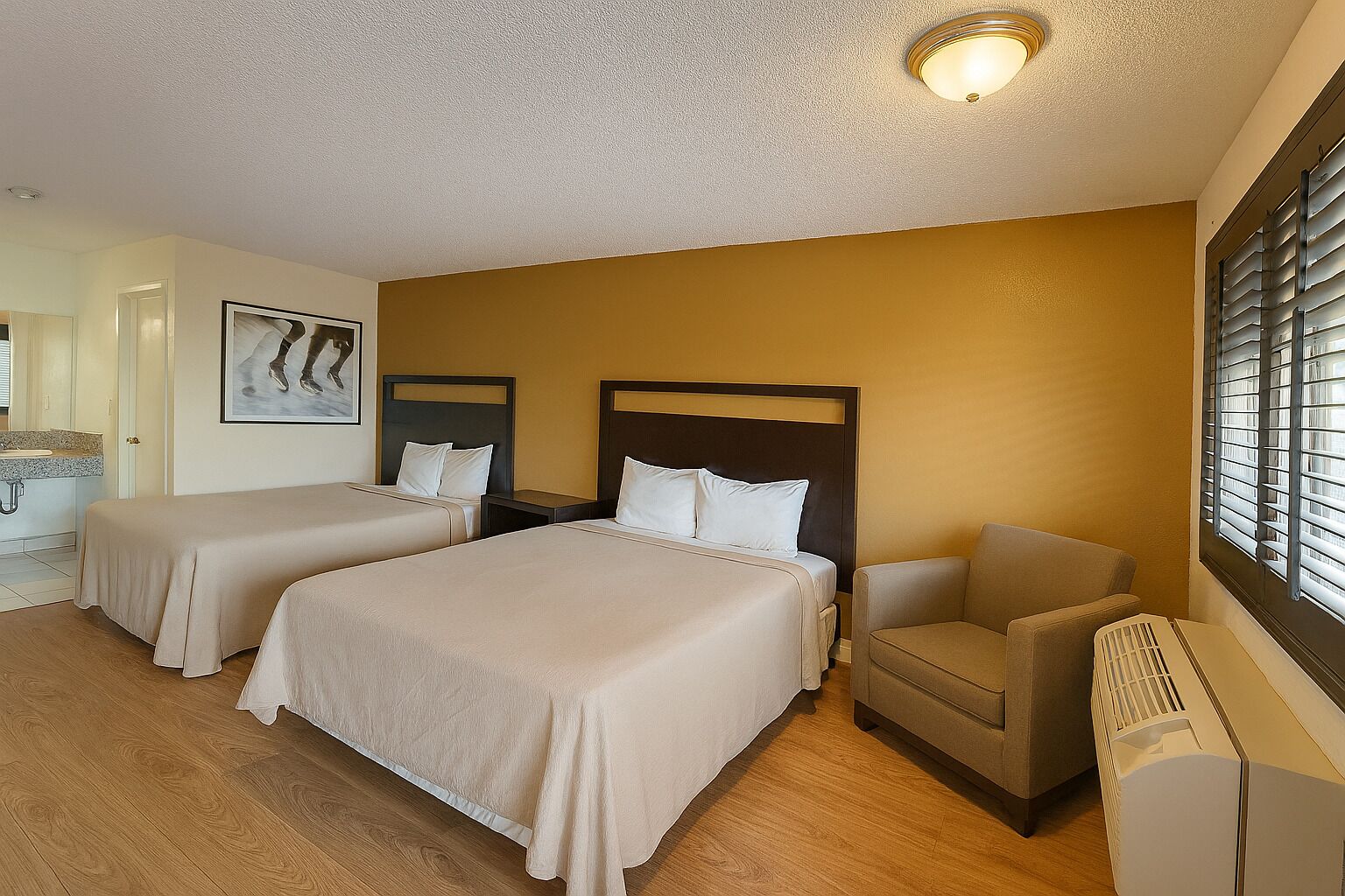 A hotel room with two beds, a chair, a radiator, and a window with blinds.