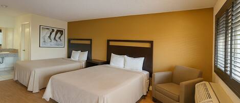 A hotel room with two beds, a chair, a radiator, and a window with blinds.