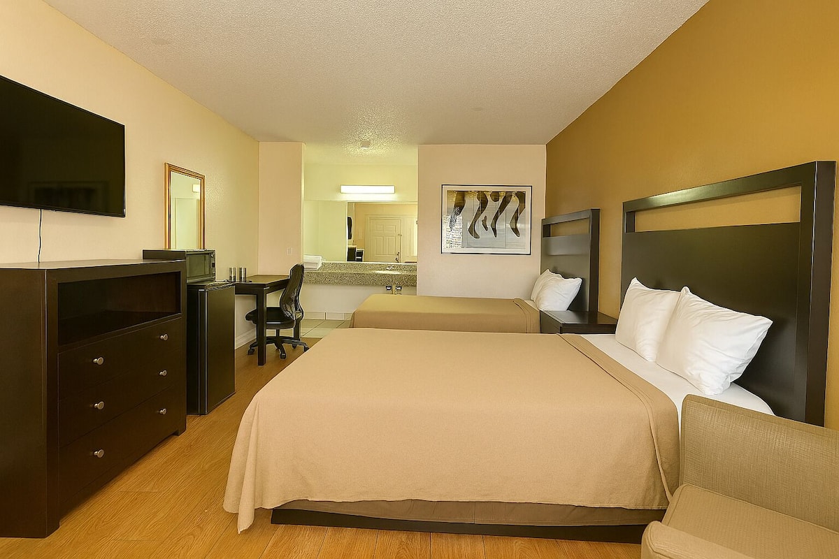 Habitación de hotel con cama, escritorio, silla, cómoda, televisor y un cuadro en la pared.