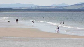 A beach with people walking along the shore and a dog near the water. - Deluxe 2 bed en-suite, stunning views, parking (Nairn)