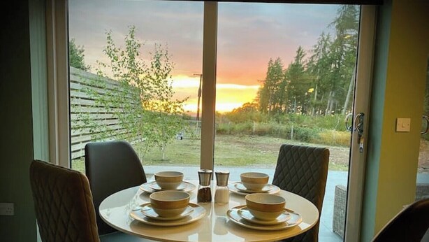 A dining table with four chairs and a view of a sunset through a glass door. - Deluxe 2 bed en-suite, stunning views, parking (Nairn)