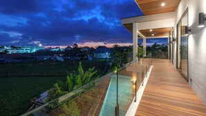 A modern building with a wooden deck and glass railings overlooking a landscaped area. - Villa Amaluna (Canggu)