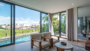 A modern living room with large windows, a pool, and a view of a residential area. - Villa Amaluna (Canggu)