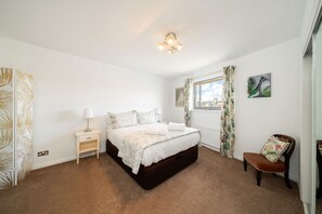 A bedroom with a bed, bedside tables, a chair, a window with curtains, and a painting on the wall.