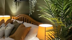 A neatly made bed with pillows and a bedside lamp, a large potted plant, and a mirror reflecting part of the room. - Beautiful 4 Bed House in Sheffield (Sheffield)