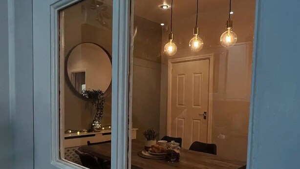 A dining area with a wooden table, chairs, hanging pendant lights, and a door in the background. - Beautiful 4 Bed House in Sheffield (Sheffield)