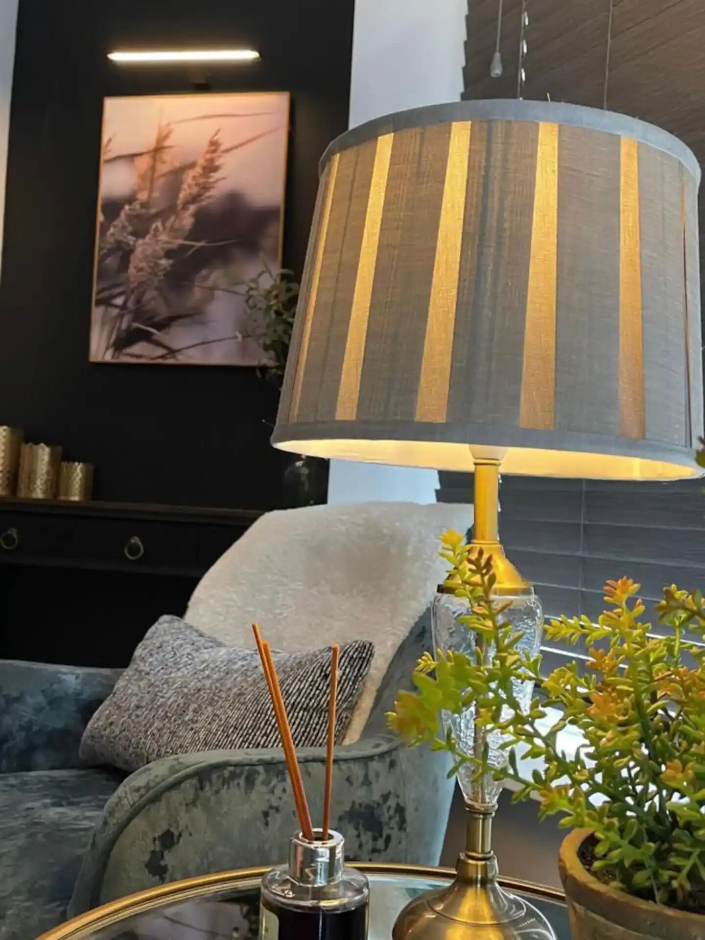 A modern living room with a striped lamp, a sofa, a decorative vase, and a framed picture on the wall.