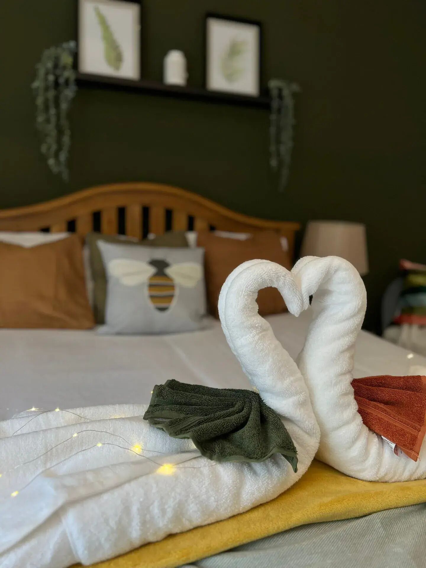 A bed with a swan-shaped towel arrangement, a wooden headboard, and a wall with framed pictures.