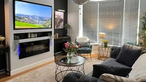A modern living room with a flat-screen TV, a large gray sofa, a coffee table, and a decorative ceiling light. - Beautiful 4 Bed House in Sheffield (Sheffield)